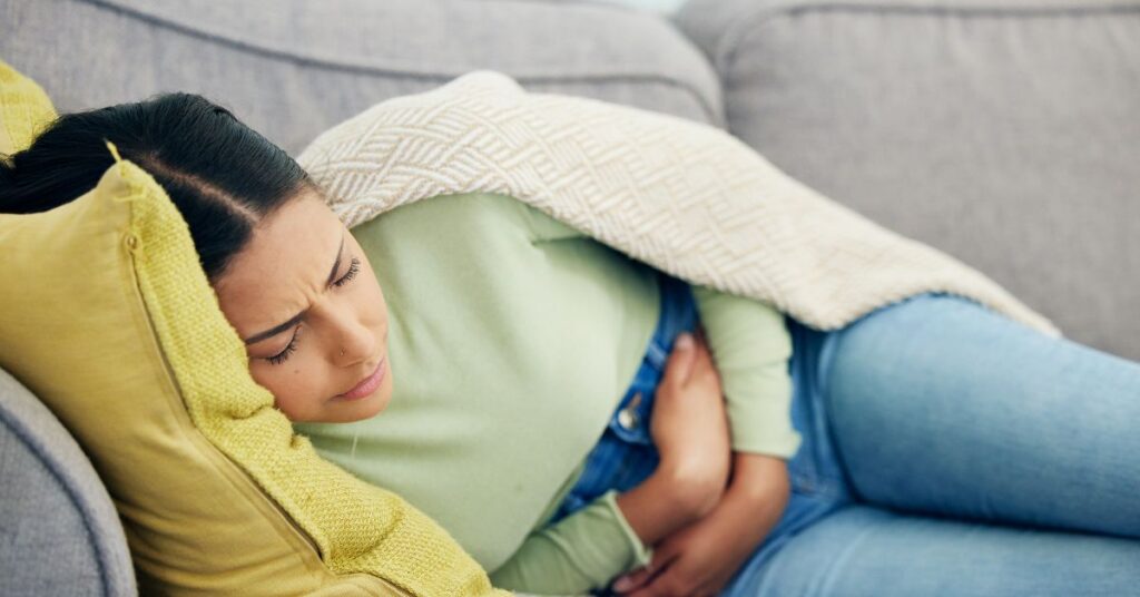 Eine Frau liegt mit Endometriose-Schmerzen auf dem Sofa